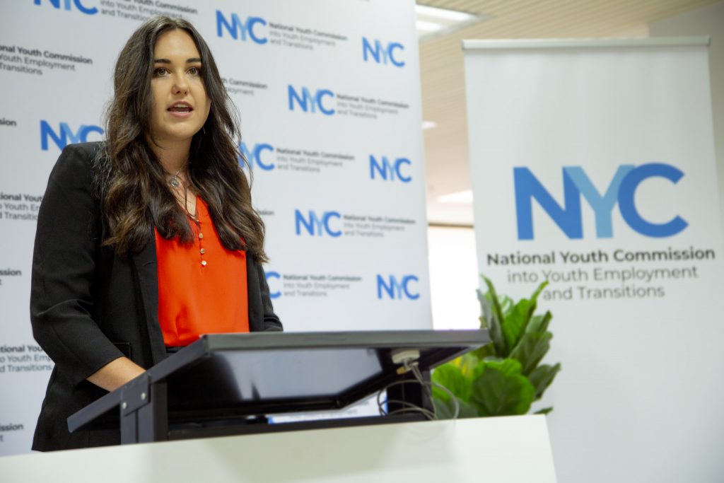 IMage of Sophie Johnston standing at a podium speaking, with a screen in the background saying NYC